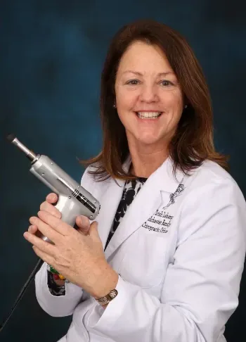 Dr. Trish in her white coat holding an Activator adjusting instrument